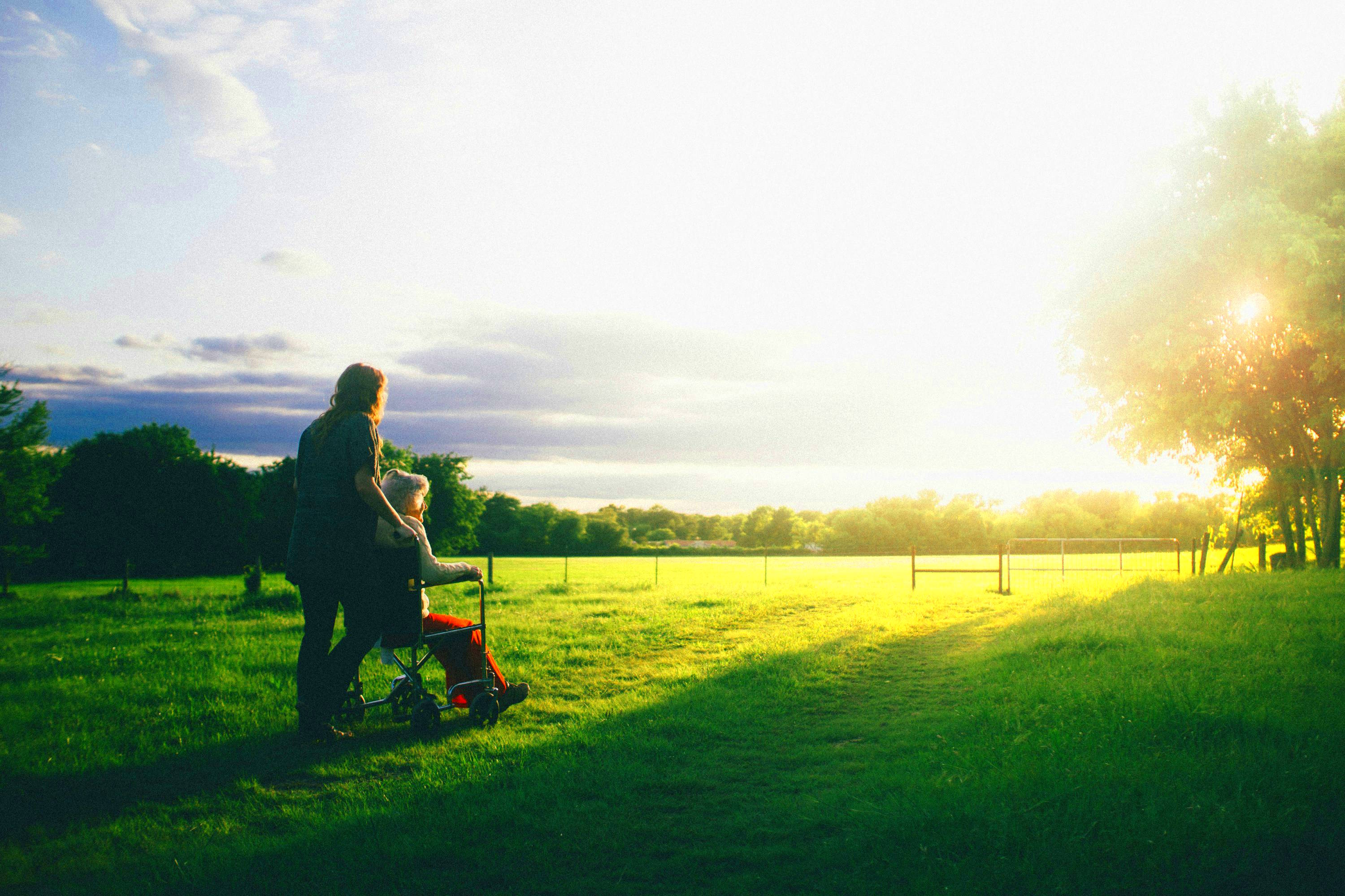 A woman pushing another woman in a wheelchair in front of a sunset